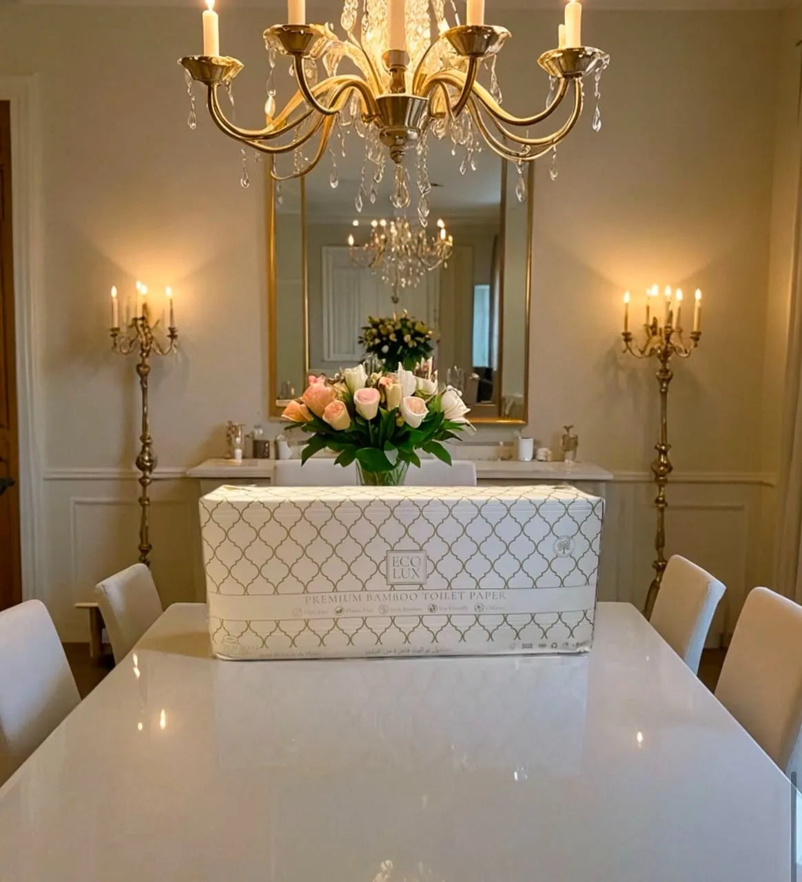 An Eco Lux case on a white dining table beneath a crystal chandelier and a vase of roses