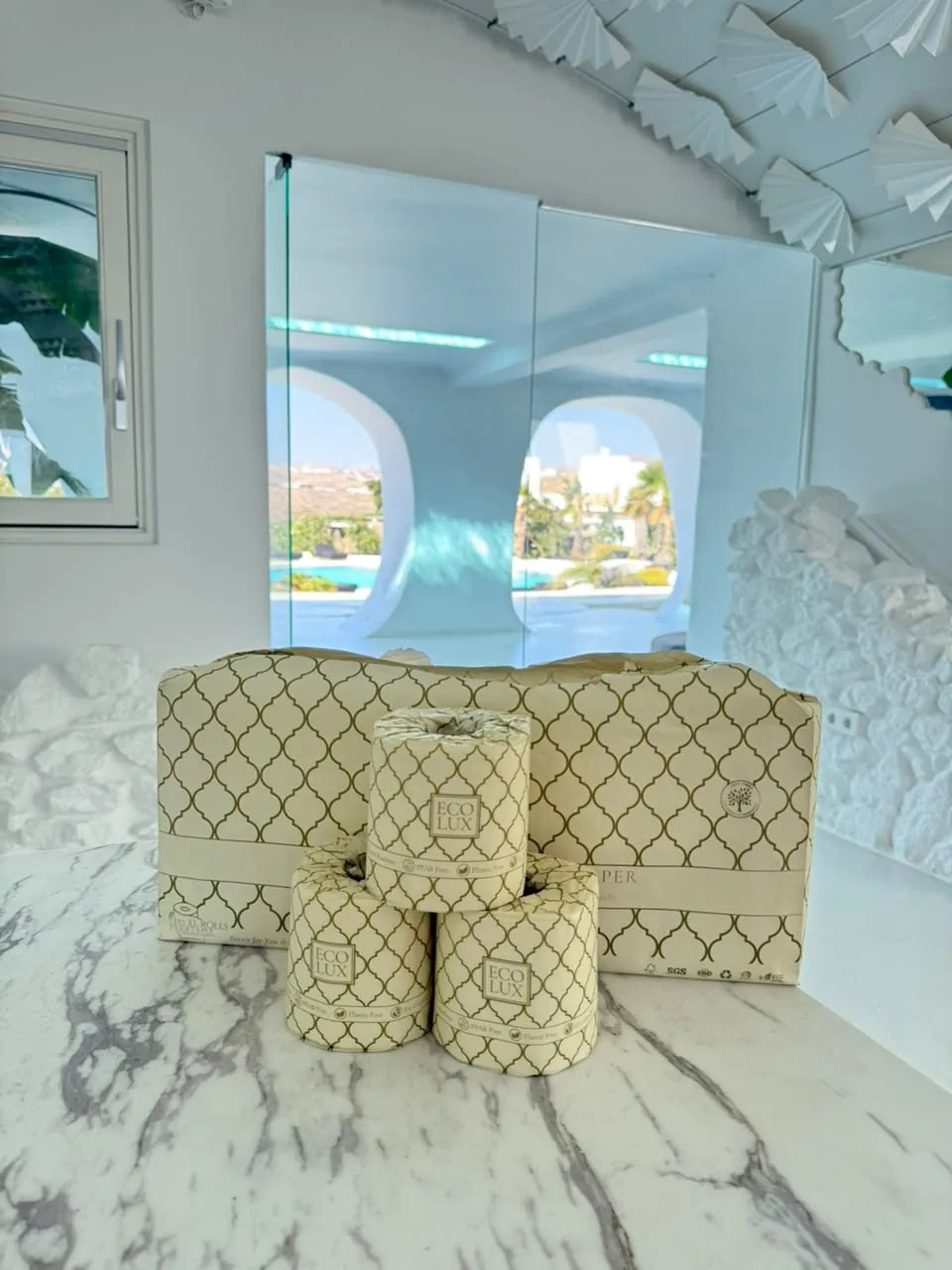 An Eco Lux case and three rolls on white marble in a bright, sculpted bathroom